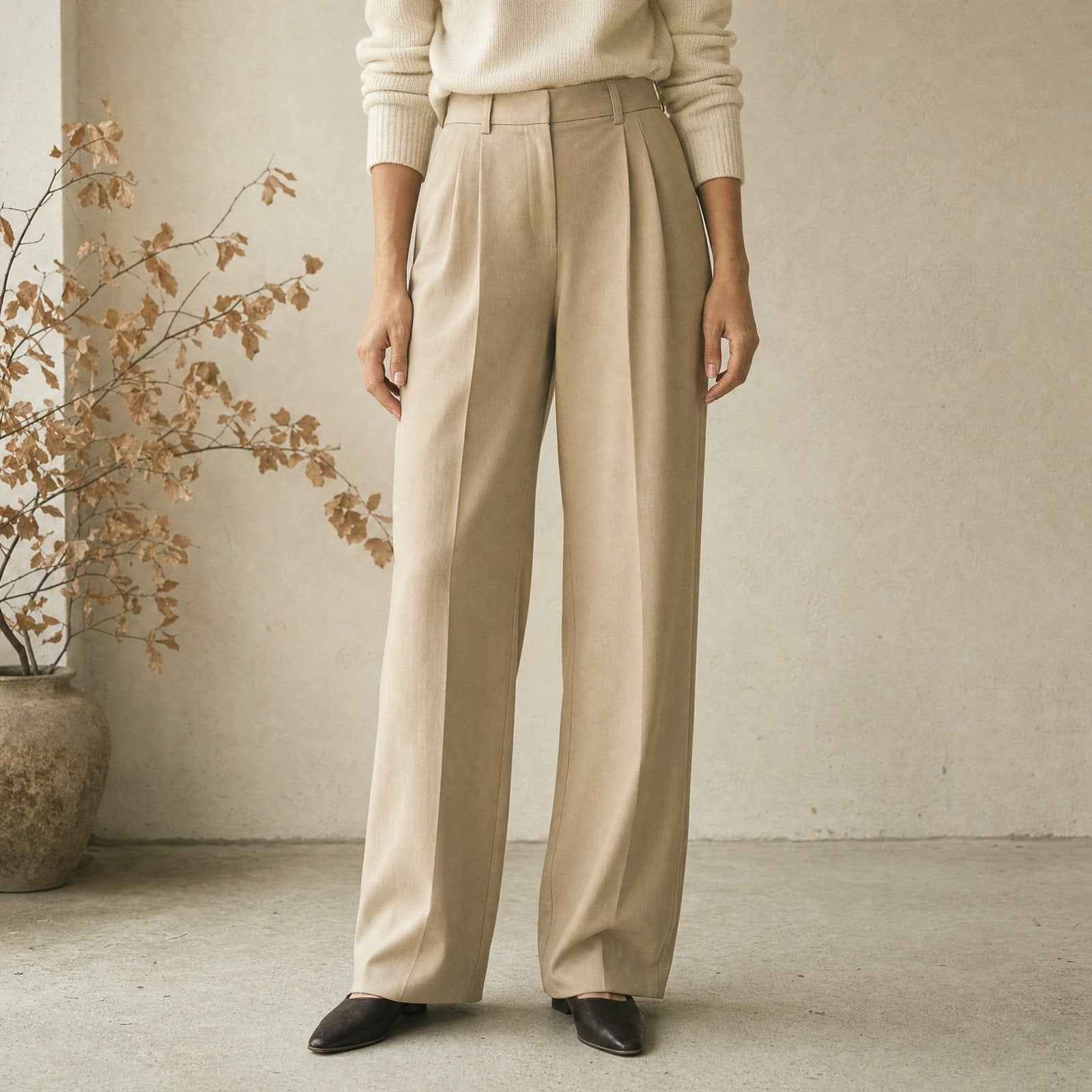 Weite Bundfaltenhose in Beige vor heller Putzwand